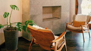 A modern living room with a flat-screen TV mounted on a stone wall, two wooden chairs with cushions, a potted plant, and a fireplace. - Atiaia Jungle River Retreat (Bocaina de Minas)