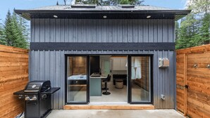 A modern, single-story building with a dark exterior, large sliding glass doors leading to an interior with a kitchen and dining area. - Luxury mini-chalets to disconnect for two with a private spa nestled in the hear (VAL DES LACS)