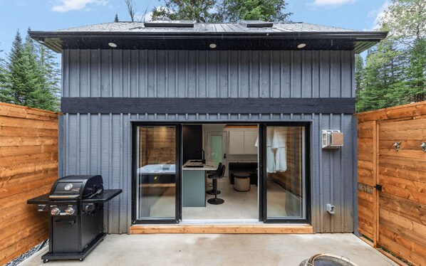 A modern, single-story building with a dark exterior, large sliding glass doors leading to an interior with a kitchen and dining area.