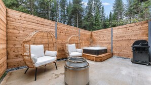 Una cabaña de madera con dos sillones de mimbre, un jacuzzi y una parrilla.