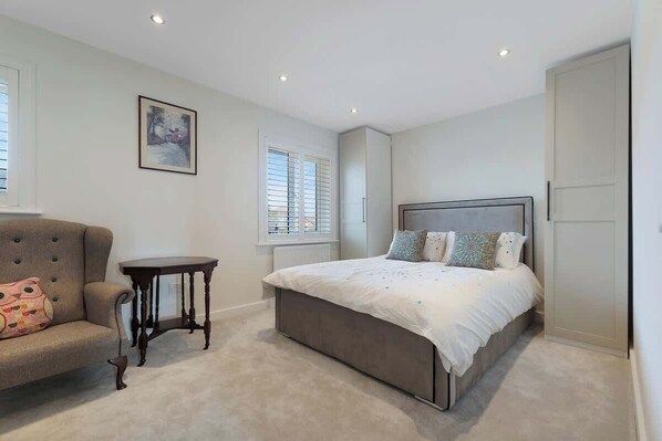A bedroom with a bed, a chair, a small table, and a picture on the wall.