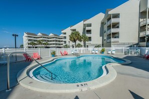 A swimming pool with a 3.5 ft depth, surrounded by a white fence, red chairs, and a building with balconies in the background. - Baywatch H3 (Pensacola Beach)