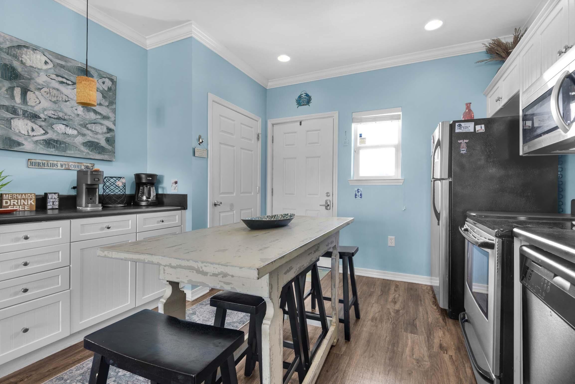 A kitchen with white cabinets, a marble island, black stools, a coffee maker, and a refrigerator.