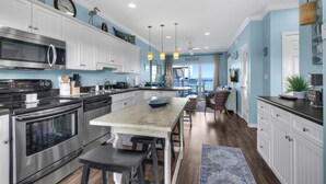 A modern kitchen with white cabinets, stainless steel appliances, and a central island. - Baywatch H3 (Pensacola Beach)