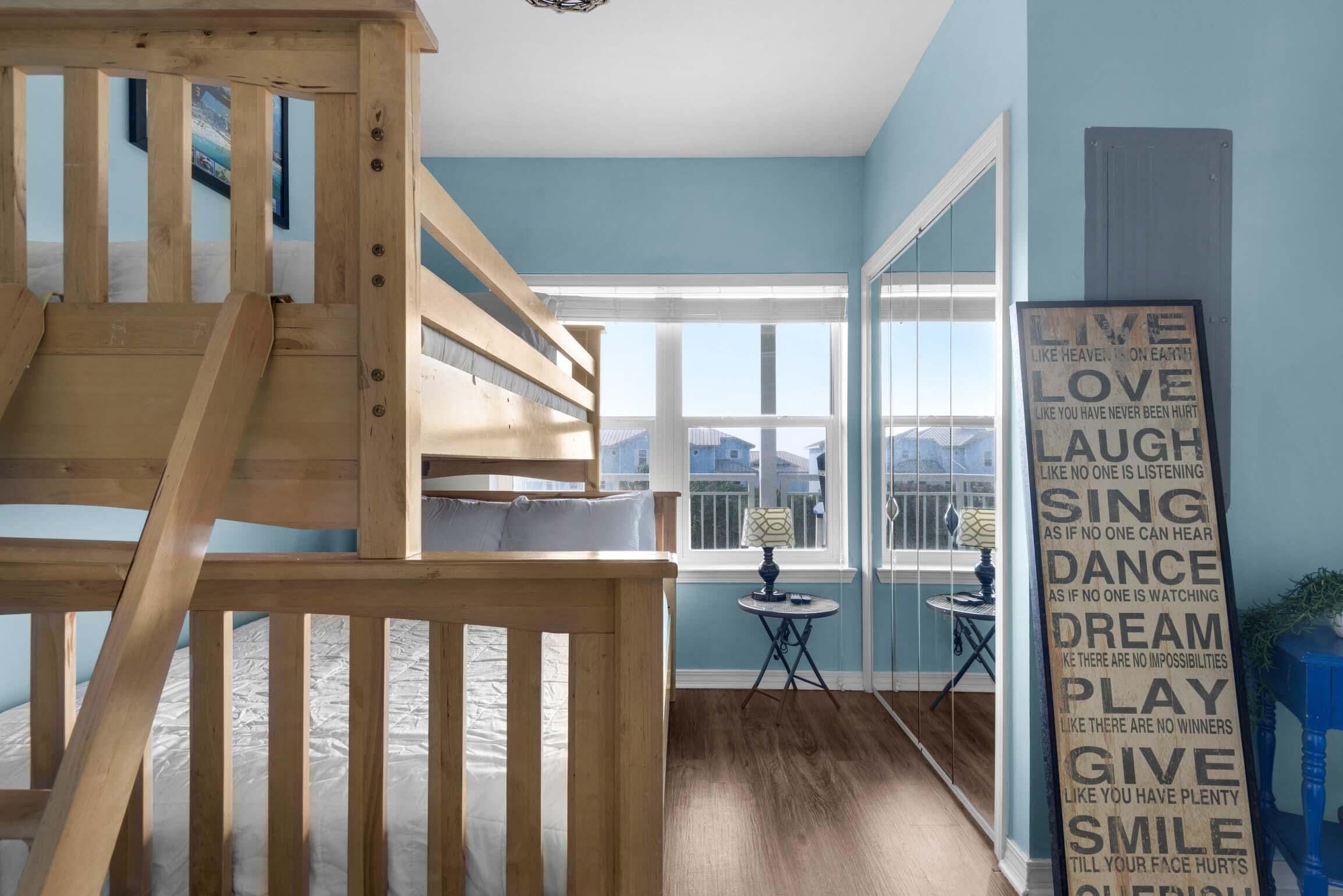 A room with bunk beds, a window with a view, a small table, and a motivational poster on the wall.