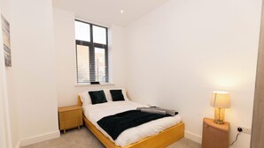 Un dormitorio con una cama de madera, una mesita de noche, una lámpara y una ventana con persianas.