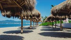 A beach with thatched umbrellas and wooden benches. - Spectacular Ocean View from 6th floor Beachfront Studio -Aria Ocean Flamingos NV (Nuevo Vallarta)