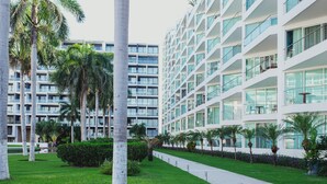 A modern hotel with multiple floors, large windows, and a well-maintained lawn with palm trees. - Spectacular Ocean View from 6th floor Beachfront Studio -Aria Ocean Flamingos NV (Nuevo Vallarta)