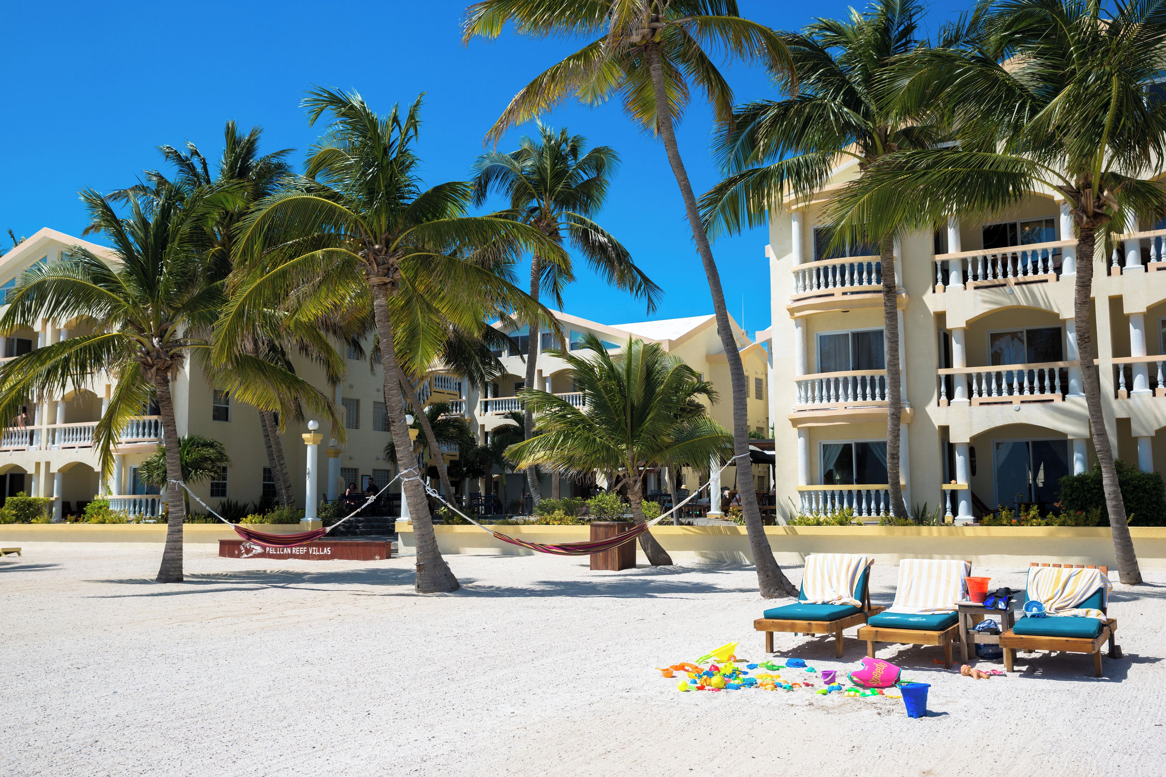 Ein Strandhotel mit mehreren Balkonen, Palmen und Liegestühlen.