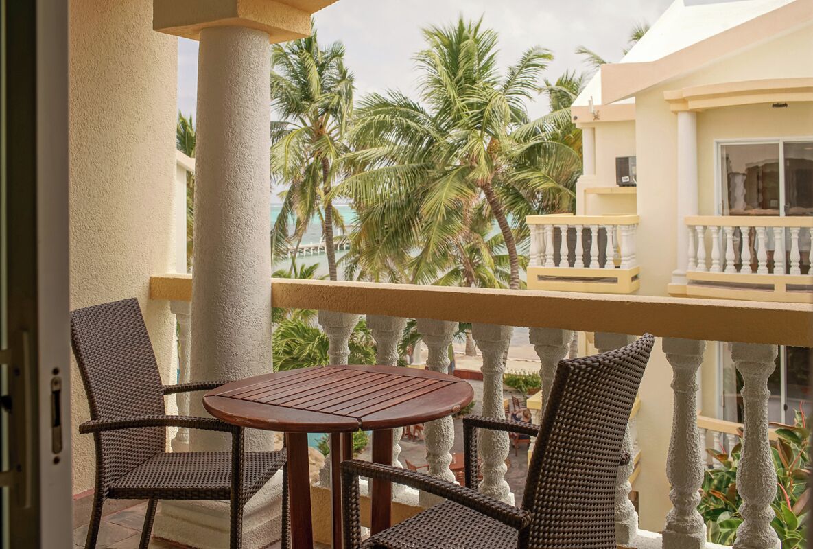 Un balcón con mobiliario de mimbre y vistas a palmeras y una piscina.