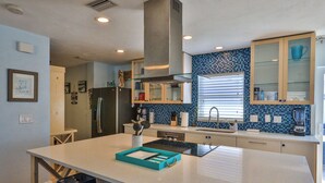 A modern kitchen with a central island, a built-in stove, and a backsplash with blue tiles. - Flip Flop Living 1 3bdrm, 2.5 bath, STEPS TO SAND! (New Smyrna Beach)