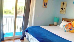 A bedroom with a bed, a ceiling fan, a window with curtains, and a view of the outdoors. - Flip Flop Living 1 3bdrm, 2.5 bath, STEPS TO SAND! (New Smyrna Beach)