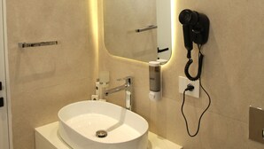 Une salle de bain moderne dotée d’un grand lavabo ovale, d’un miroir avec éclairage intégré, d’un sèche-cheveux et d’un distributeur de papier toilette.