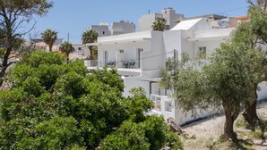 Edifici modern i blanc amb balcons, envoltat de verdura i altres edificis.