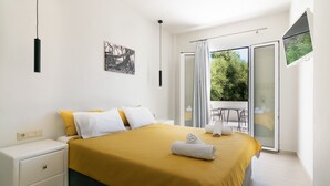 A modern bedroom with a large bed, a nightstand, a painting, and a balcony with a table and chairs. - Secretnest 15, apartment near the beach,Plakias (Plakias)