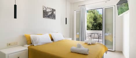 A modern bedroom with a large bed, a nightstand, a painting, and a balcony with a table and chairs.
