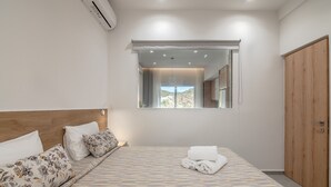 A bedroom with a bed, a wooden wardrobe, a window with a view, and an air conditioning unit.