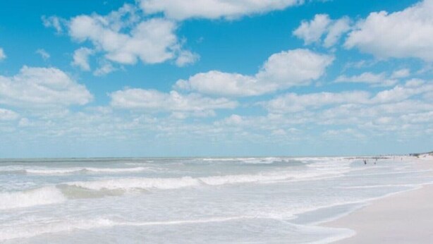 Una playa con olas, cielo despejado y un muelle a lo lejos.