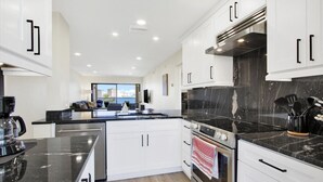 Una cocina moderna con armarios blancos, encimeras negras y electrodomésticos de acero inoxidable.