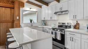 A modern kitchen with white cabinets, a large island, stainless steel appliances, and wooden beams on the ceiling. - Mid-Century Nest, Near Forest Park (Portland)