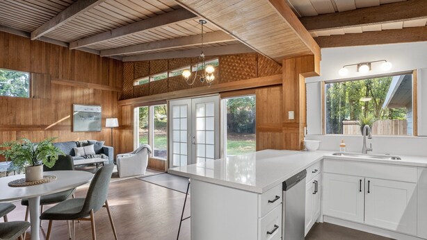 A modern kitchen with white cabinetry, a large island, and a dining area with a table and chairs. - Mid-Century Nest, Near Forest Park (Portland)