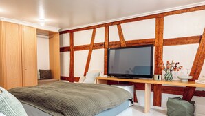 Un dormitorio con cama, televisor, escritorio con un florero y vigas de madera en el techo.