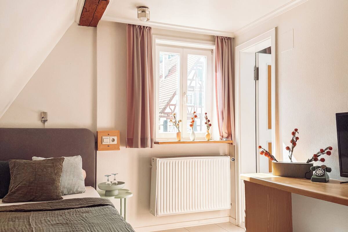 Un dormitorio con cama, escritorio, radiador y ventana con cortinas.