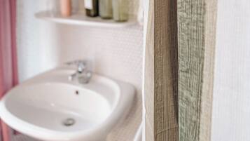 A bathroom with a white sink, a mirror, and a shelf with bottles.