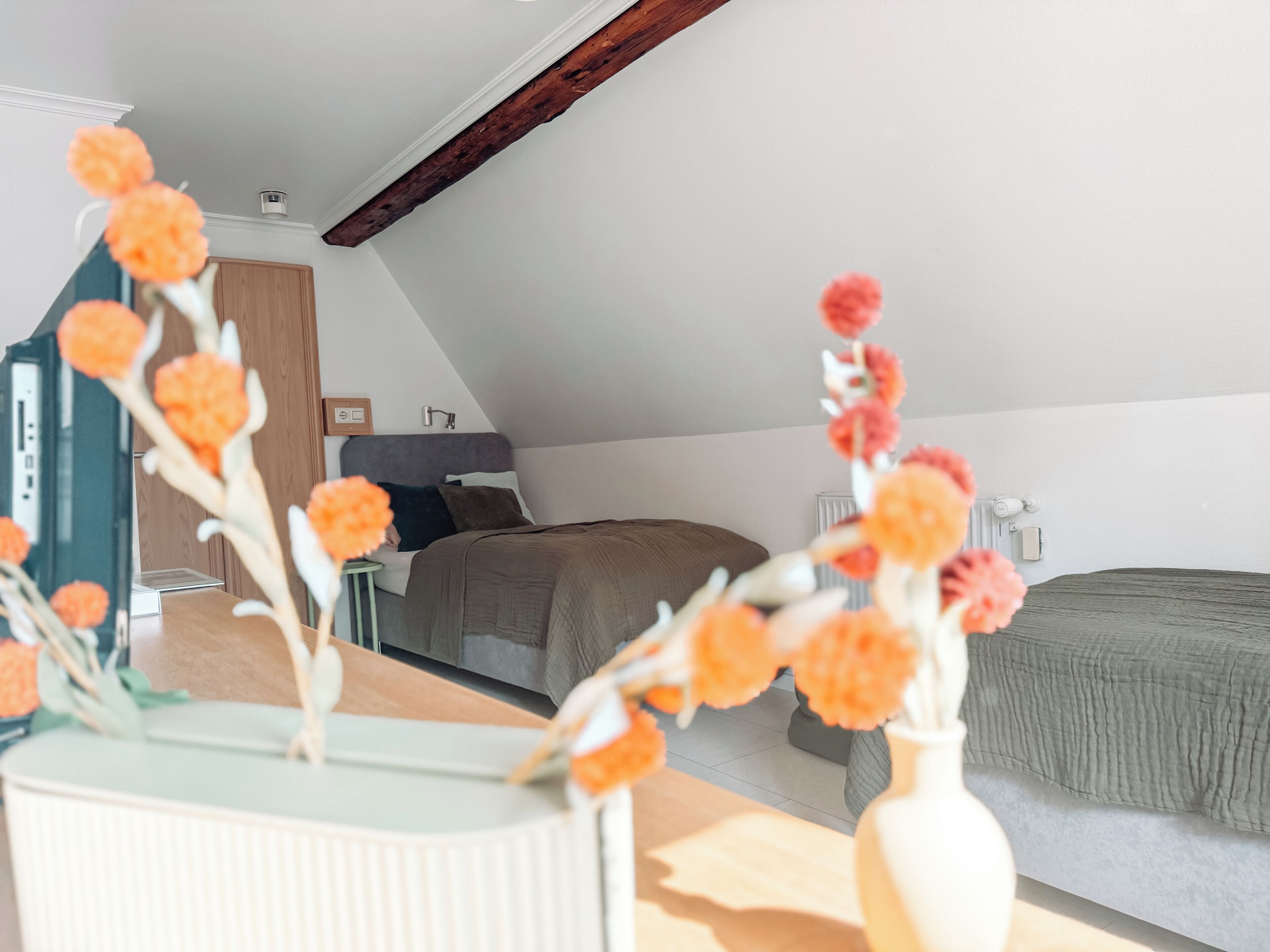 A modern bedroom with a sloped ceiling, a bed with a dark headboard, and a bedside table with a vase of flowers.
