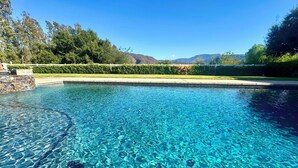 Una piscina cristalina con borde de piedra y vistas a montañas al fondo.