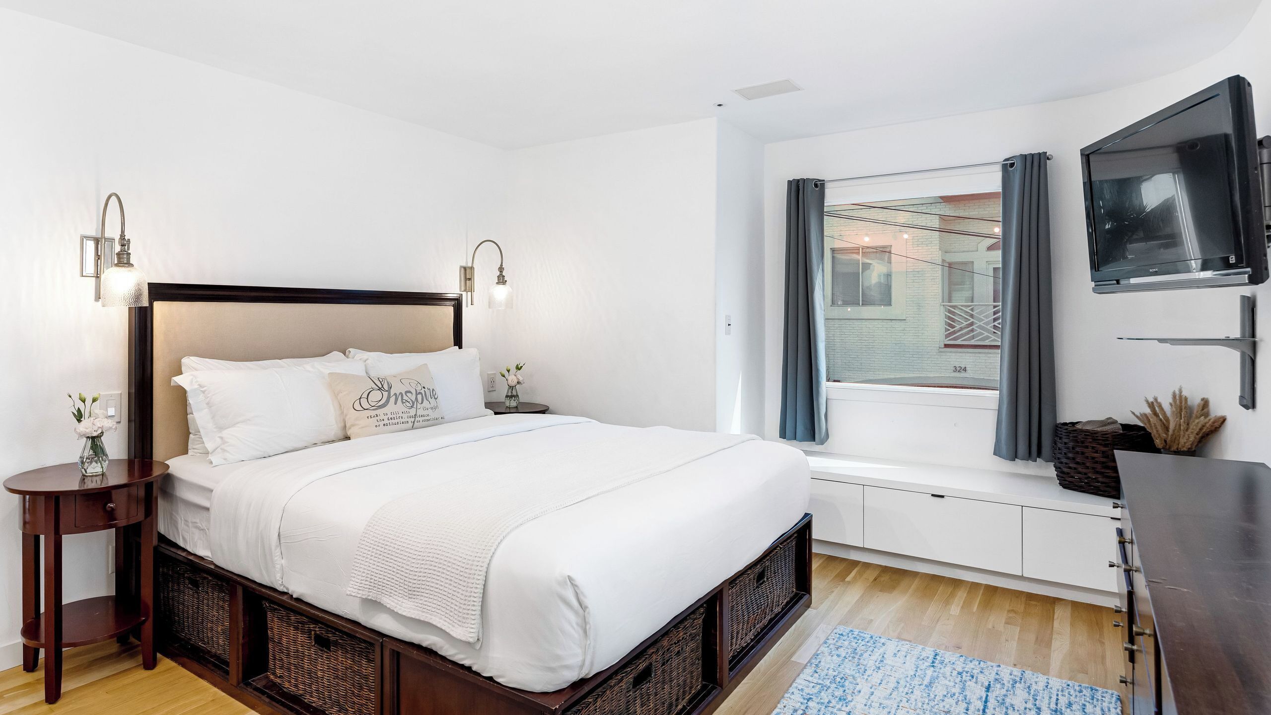 A neatly arranged bedroom with a bed, bedside tables, a TV, and a window with curtains.
