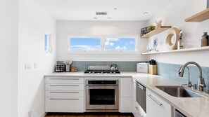 A modern kitchen with a gas stove, oven, dishwasher, and a window with a view of the sky.