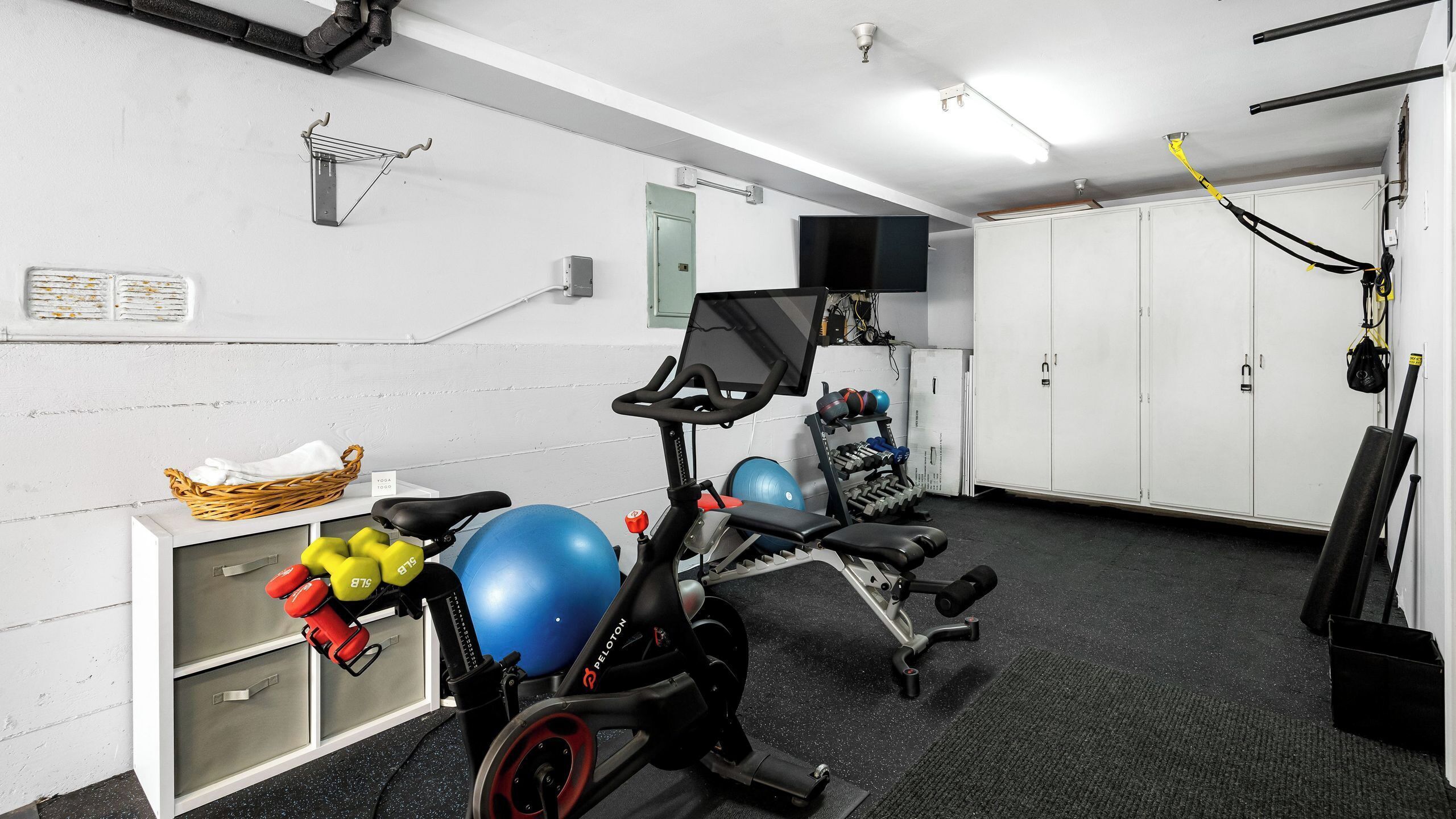 Un gimnasio con equipamiento de ejercicio, un estante en la pared y una cesta con toallas.