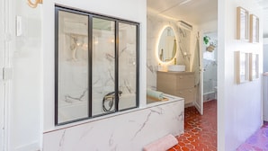A modern bathroom with a large glass shower enclosure, a marble vanity, and a mirror with an oval frame.