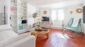 A living room with a white sofa, a green chair, a round coffee table, and a TV on a stand.