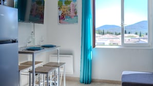 A kitchen with a refrigerator, a dining table with chairs, a window with a view of buildings and mountains, and a poster on the wall.