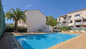 A swimming pool with a tiled deck, surrounded by buildings with balconies and a palm tree.