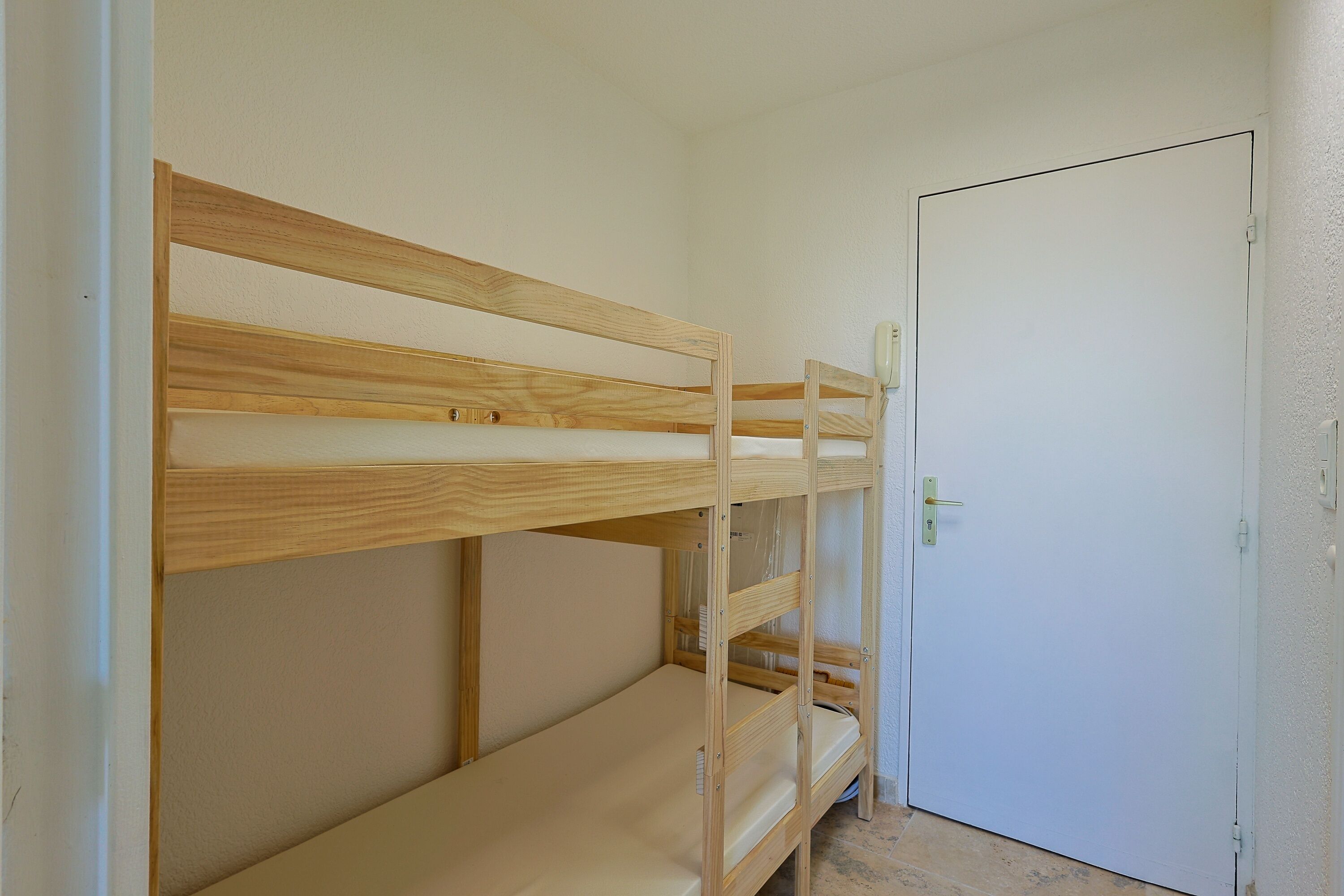 Un lit superposé dans une pièce avec une porte blanche et des murs unis.