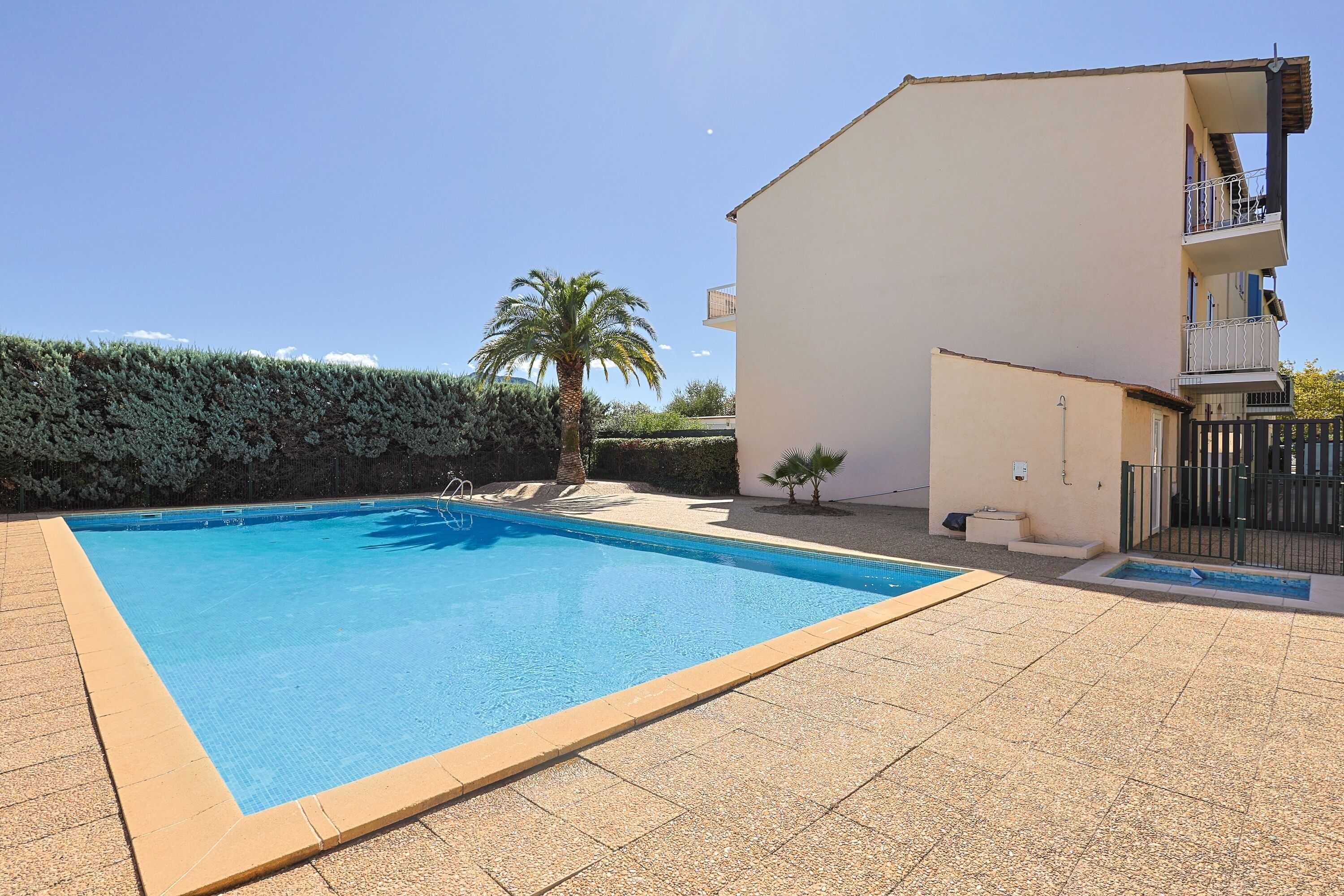 Une piscine rectangulaire dont le bord est recouvert de carreaux, entourée d’une zone dallée.