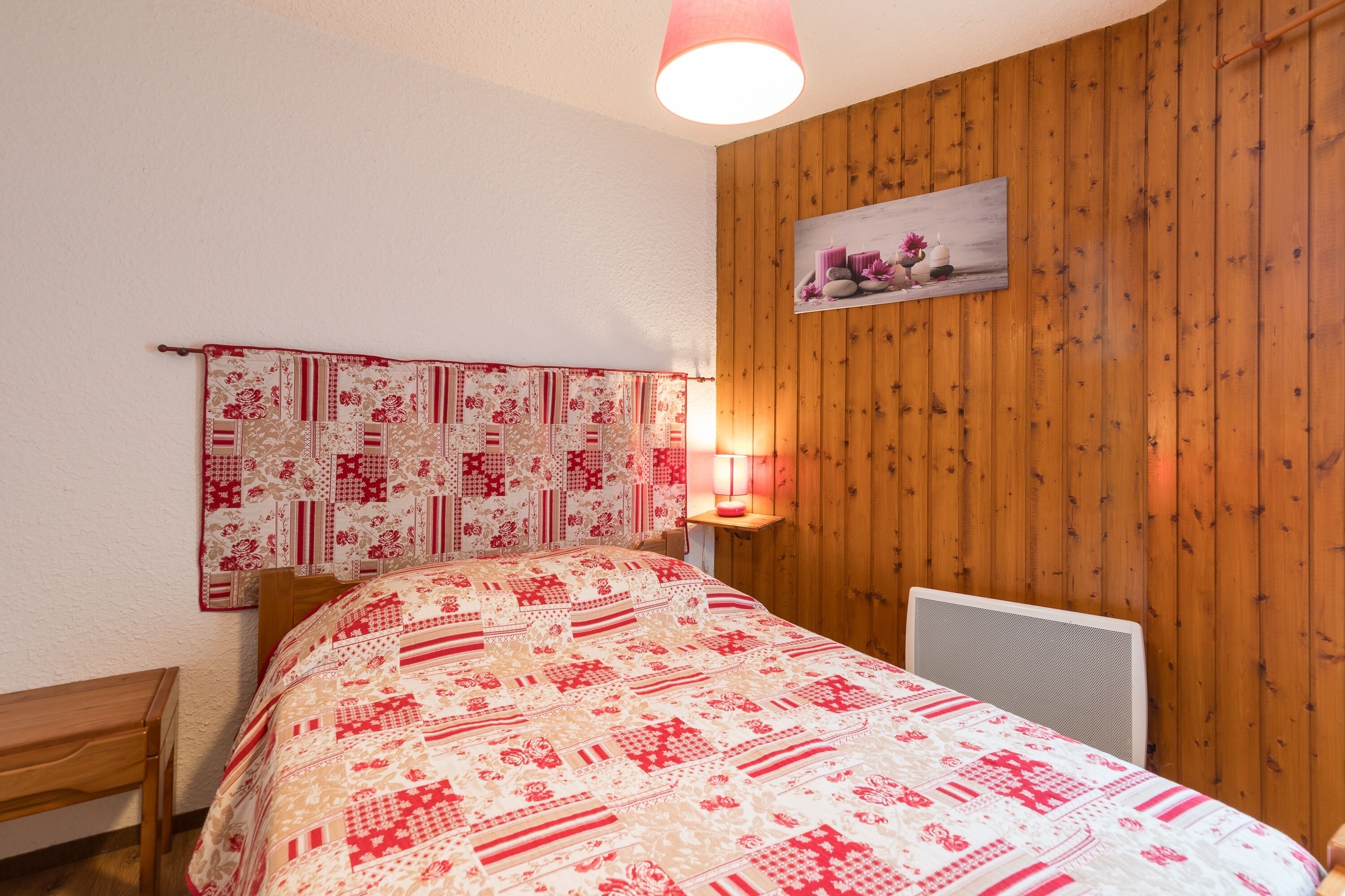Un dormitorio con pared de madera, colcha acolchada, mesita de noche y lámpara de pared.
