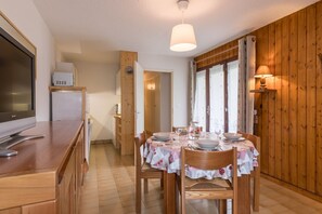 Un comedor con paredes de madera, una mesa de madera dispuesta para cuatro comensales y un televisor sobre un mostrador de madera.