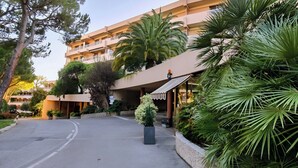 Ein mehrstöckiges Hotel mit überdachter Einfahrt, umgeben von üppiger Vegetation und Palmen.