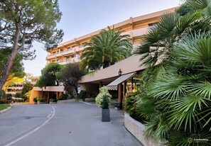 Ein mehrstöckiges Hotel mit überdachter Einfahrt, umgeben von üppiger Vegetation und Palmen.
