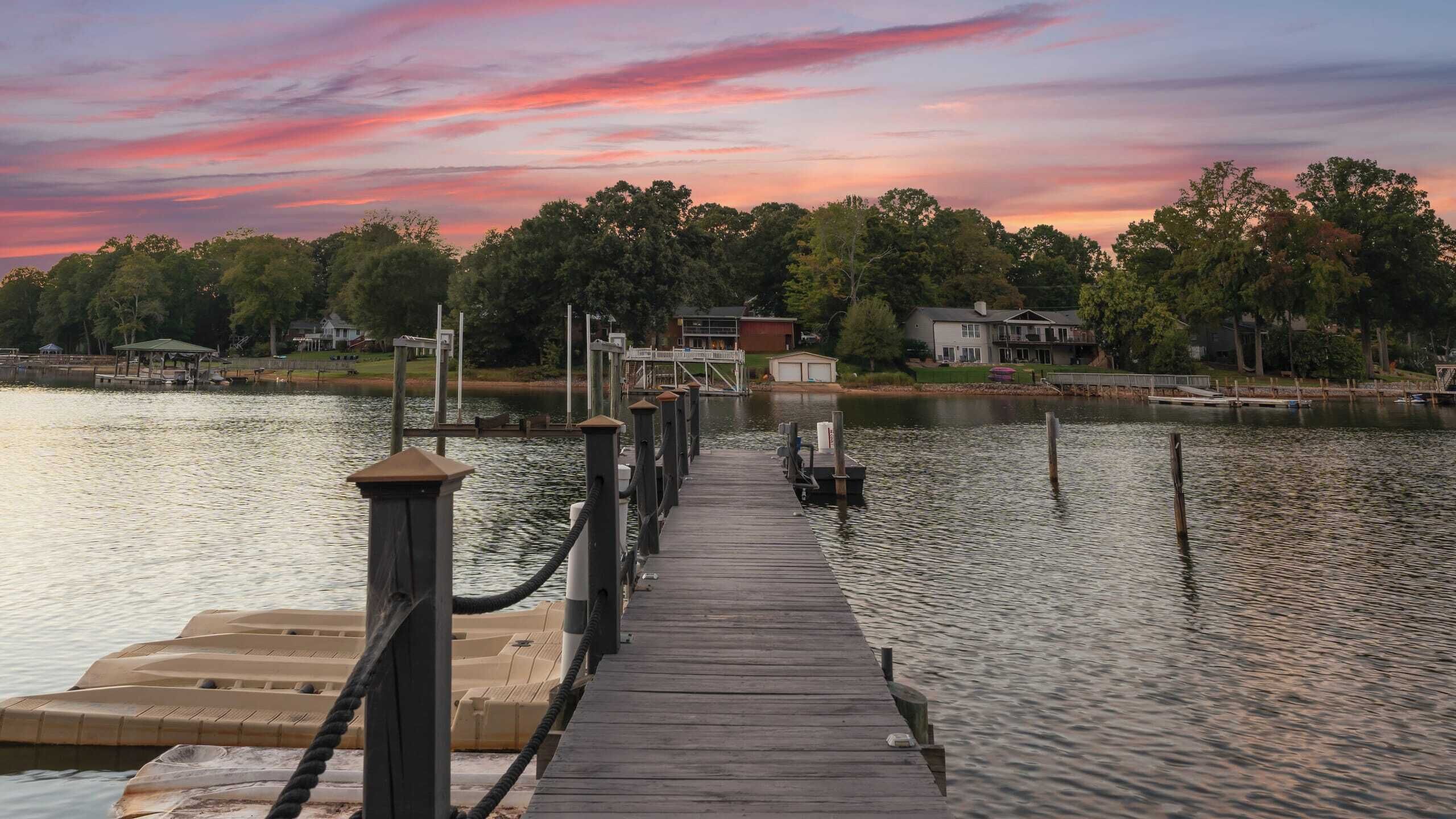 A wooden pier extending into a lake with houses and trees in the background.