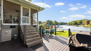 Une terrasse dotée de mobilier d’extérieur, d’un escalier couvert et offrant une vue sur un lac où naviguent des bateaux.