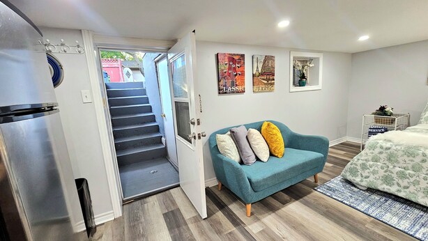 Ein kompakter Wohnbereich mit Küchenzeile, einer Couch mit Kissen, einem Bett und einer Treppe, die zu einem Außenbereich führt.