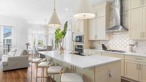 A modern kitchen with a central island, bar stools, pendant lighting, and a view to the outside.