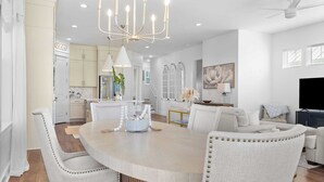 A spacious living room with a large round table, comfortable seating, and a modern chandelier.