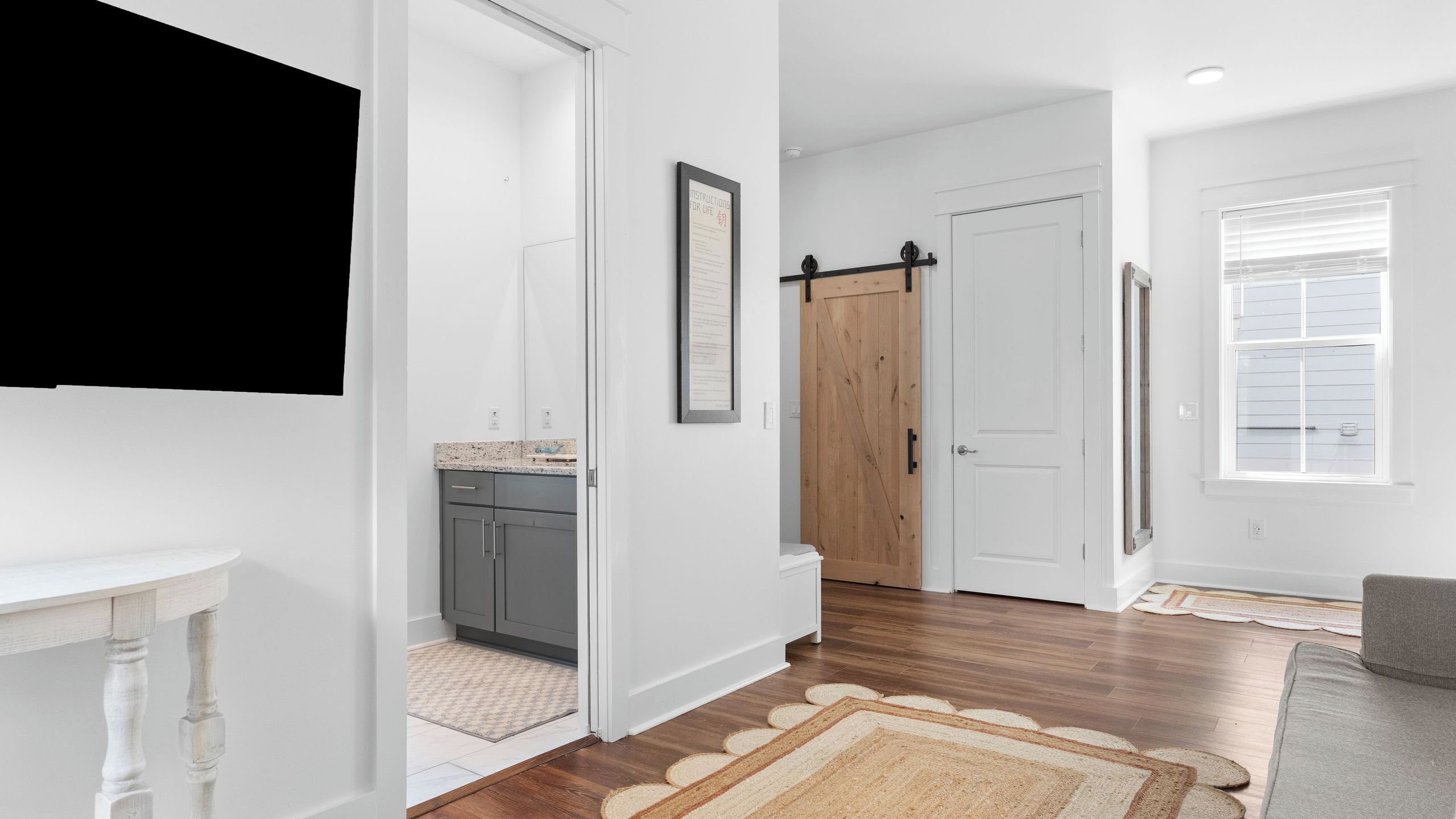 Un pasillo con cocina, una puerta de madera, una puerta blanca y un ventanal con persianas.