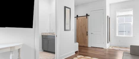 Un pasillo con cocina, una puerta de madera, una puerta blanca y un ventanal con persianas.